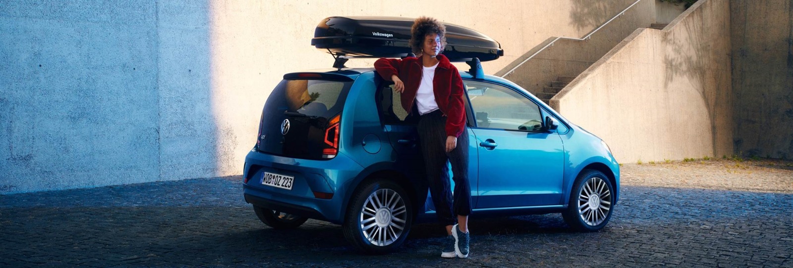 Blauwe Volkswagen Up! Met Een Vrouw Die Er Op Leunt